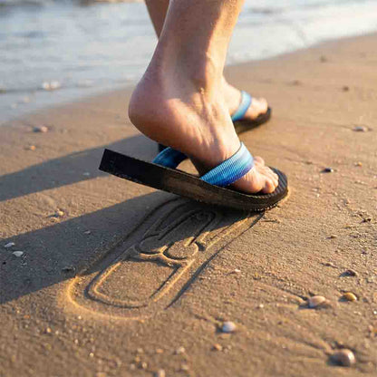 Close-up of a foot stepping in a Soleprint flip-flop, leaving a print in wet sand